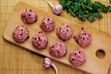 raw meatballs on a cutting board on a background of a bamboo mat with garlic and parsley