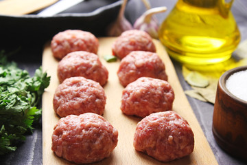 close up raw meatballs on a cutting board on a background of a bamboo mat with garlic and parsley