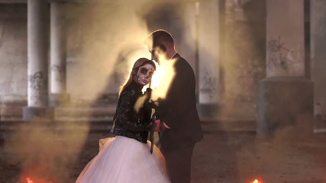 Couple with dark skull makeup on the background of burning fire and smoke. Halloween face art. Halloween concept. Zombie. Silhouette. Slow motion.