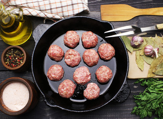 raw meatballs in reying pan onblack bodges table top with fabric napking fork and spoon, spices salt oil and seasoning copy space flat lay