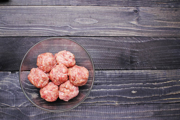flat lay raw meat balls in a glass bowl on  black wooden table top close up copy space