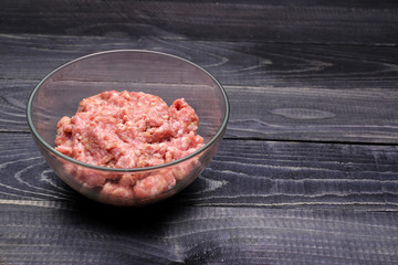 raw minced meat in glass bowl on black wooden table top surface. Burger. 