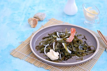 Light kelp, onion and shrimp salad on a brown clay plate. Served with mayonnaise sauce. Laminaria salad. Copy space.