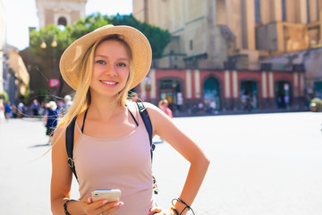 Europe travel summer tourism holiday vacation background - young attractive Caucasian smiling beautiful blonde girl face with hat mobile cell phone and using backpack in hand having chat in city