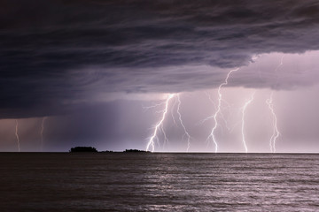 Several lightning strikes the sea not far from a small island, clouds in the sky, waves on the...