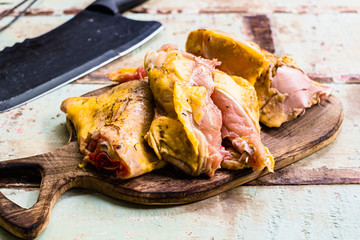 Pieces of fresh raw chicken parts on a cutting board on wooden old plank or table with black knife.
