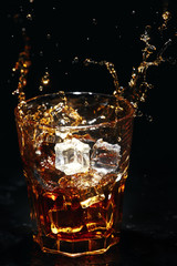 Whiskey alcogol drink splash with ice on a dark background