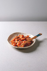 Cutting salmon fish soy sauce marinated in ceramic plate with wooden chopsticks on grey kitchen table. Copy space.