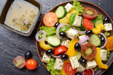 Top view at Mediterranean diet dish greek salad on slate tray with sauce aside