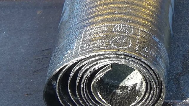 Worker preparing part of bitumen roofing felt roll for melting by gas heater torch flame. On the back of the sheath there is the stamp  "Made in Italy" product