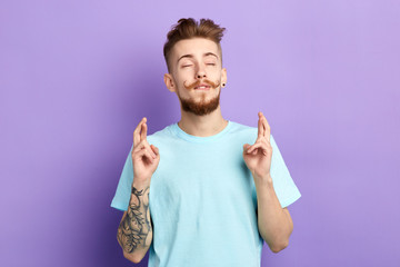 Handsome man with closed eyes wishes to win the lottery, student want to pass exams, faithful man pleading the God to start up successful business, isolated blue background , studio shot