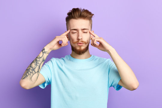 Young relaxed man concentrating on thoughts,suffering from headache, pressing fingers to temples, isolated on blue background. relaxation, man massaging his temples. guy trying to remember some facts