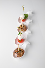 Assorted canapes on caprese skewers with cherry, mozzarella and basil and meatballs. Beautifully decorated catering banquet menu. Food snacks and appetizers for buffet. Isolated on white background