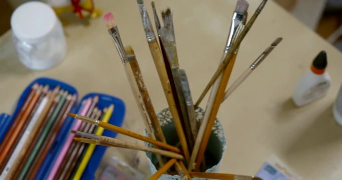 artistic brushes and pencils are inside jars standing in work table in studio of painter, detail view