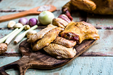 Pieces of fresh raw chicken parts on a cutting board on wooden old plank or table with blur Thai herbs and whole chicken. Chicken with Thai herbs prepared for cooking soup.