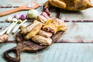 Pieces of fresh raw chicken parts on a cutting board on wooden old plank or table with blur Thai herbs and whole chicken. Chicken with Thai herbs prepared for cooking soup.