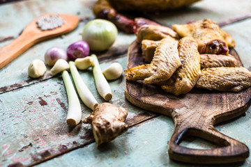 Pieces of fresh raw chicken parts on a cutting board on wooden old plank or table with blur Thai herbs and whole chicken. Chicken with Thai herbs prepared for cooking soup.