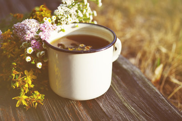 Herbal tea in an iron cup white yarrow flowers and St. John's Wort flowers on old wooden surface, soft focus, toned. Tea and herbs, alternative medicine