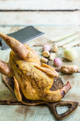 Whole fresh raw chicken on a cutting board on wooden old plank or table with blur Thai herbs and whole chicken. Chicken with Thai herbs prepared for cooking soup.