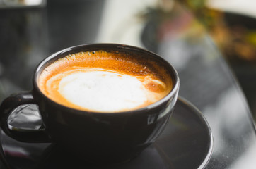 close up modern hot black coffee the cappuccino on dark background with coffee bubble foam pattern and texture in black cup looking and feel so delicious on glasses table in coffee shop.