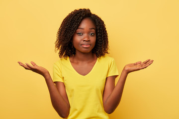good looking puzzled woman doubting and shrugging shoulders isolated over yellow background. studio...