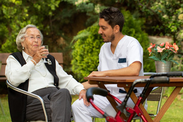 Senior woman drinking water next to male nurse in garden.
