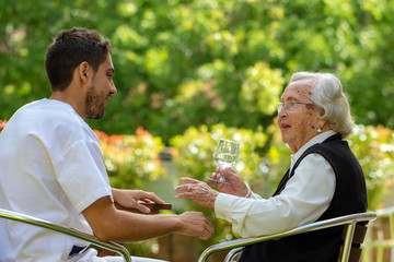 Senior woman having conversation with young male nurse in garden.