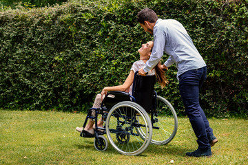 Young man pushing disabled girl in wheelchair outdoors.