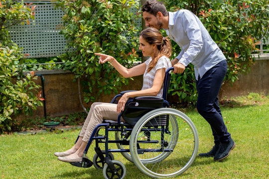 Young handicapped woman in wheelchair enjoying time with male friend in park.