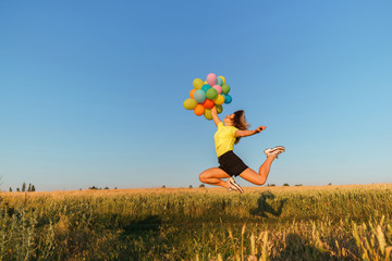 follow your dream, inspiration concept, young woman with colorful balloons jumping in summer field. fun, vacation, bright life