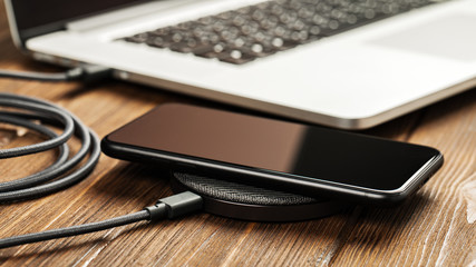 Wireless charging lies next to the computer on a stylish wooden table