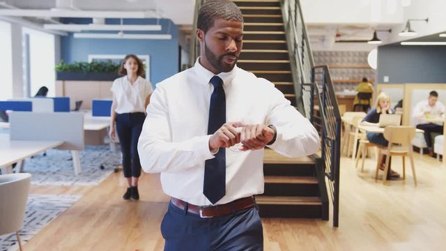 Businessman Walking Through Modern Office Checking Data On Smart Watch
