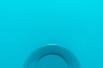 Minimalist image of round ceramic plate over turquoise blue background with copy space. Top view of blank dish on blue table central composition.