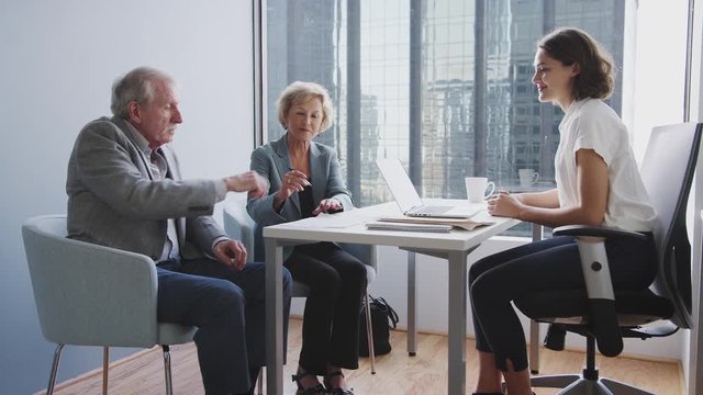 Senior Couple Signing Document In Meeting With Female Financial Advisor In Office