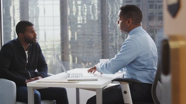 Man Meeting With Male Financial Advisor In Office And Discussing Document