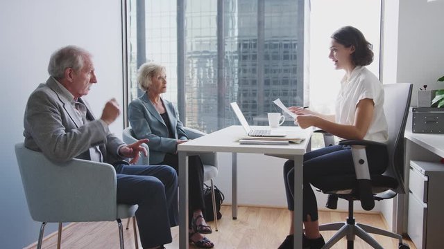 Senior Couple Signing Document In Meeting With Female Financial Advisor In Office