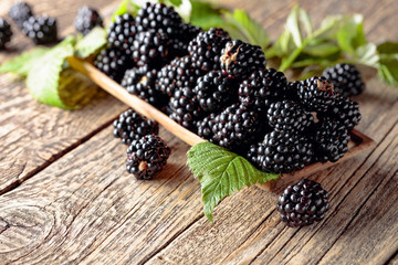 Ripe juicy blackberries with leaves on a wooden table.