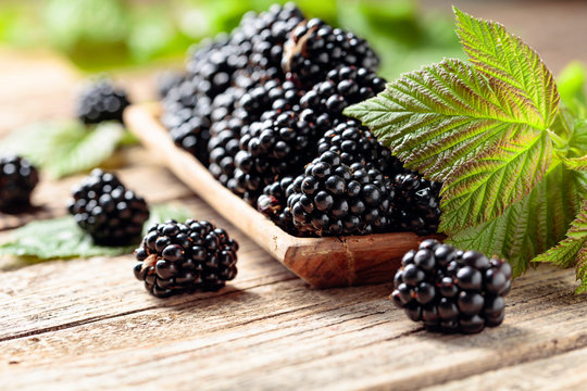 Ripe juicy blackberries with leaves on a wooden table.