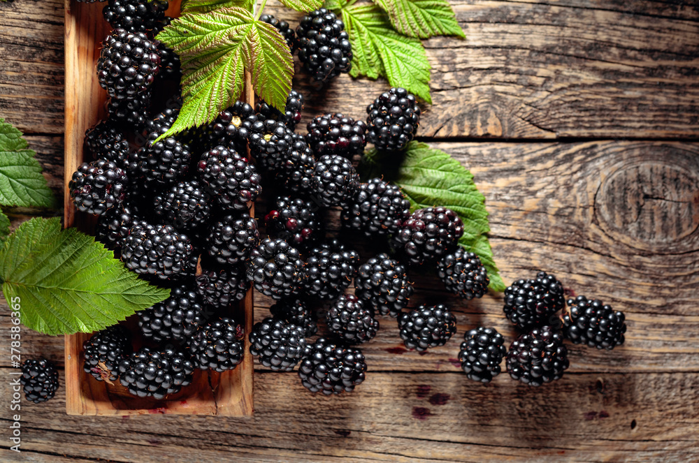 Wall mural ripe juicy blackberries with leaves on a wooden table.