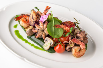 Luxurious seafood salad with shrimp, octopus, squid, fish, lime, cherry tomatoes, grilled vegetables and greens Banquet festive dishes. Fine dining restaurant menu. White background.