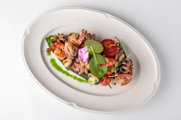 Luxurious seafood salad with shrimp, octopus, squid, fish, lime, cherry tomatoes, grilled vegetables and greens Banquet festive dishes. Fine dining restaurant menu. White background.