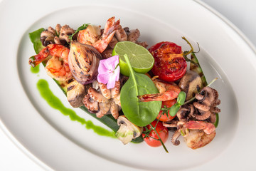 Luxurious seafood salad with shrimp, octopus, squid, fish, lime, cherry tomatoes, grilled vegetables and greens Banquet festive dishes. Fine dining restaurant menu. White background.