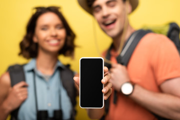 selective focus of cheerful woman showing smartphone with blank screen while standing near smiling man on yellow background