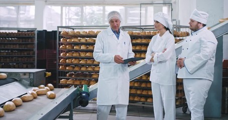 Old man engineer explaining to the baker chef big man and his assistance the rules of using the automated conveyor line , they wearing special uniform