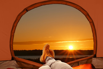 Closeup of man in camping tent near river at sunset, view from inside