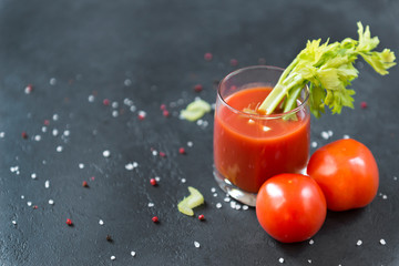 tomato juice with fresh tomatoes and celery stalk and spices on black background