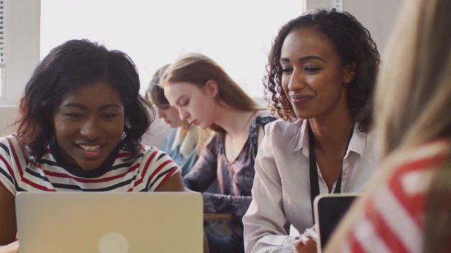 Woman Teacher Giving One To One Support To Female Student Working At Desk On Laptop