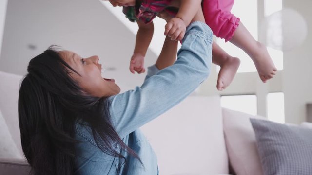 Mother Playing With Baby Daughter Lifting Her In The Air At Home
