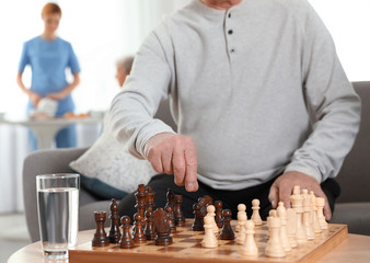 Elderly men playing chess at nursing home, closeup. Assisting senior people