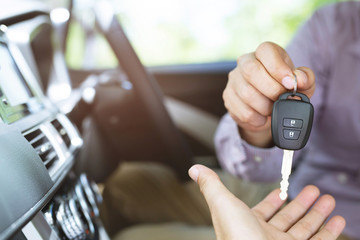 Car key, businessman handing over gives the car key to the other man in car interior background....